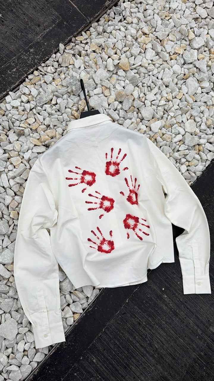 White jacket with red handprint designs on a gravel surface