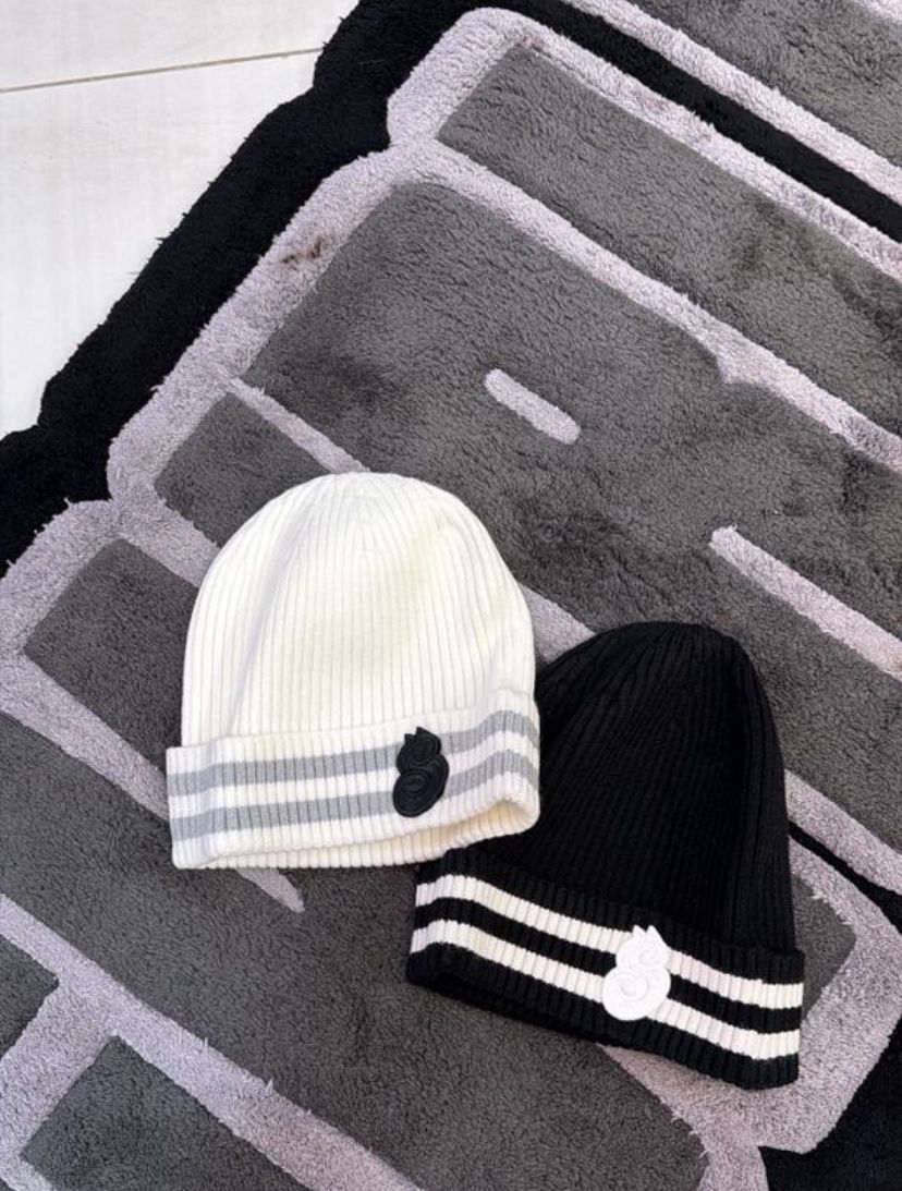 Two knit hats, one white and one black, with stripes on a textured surface.