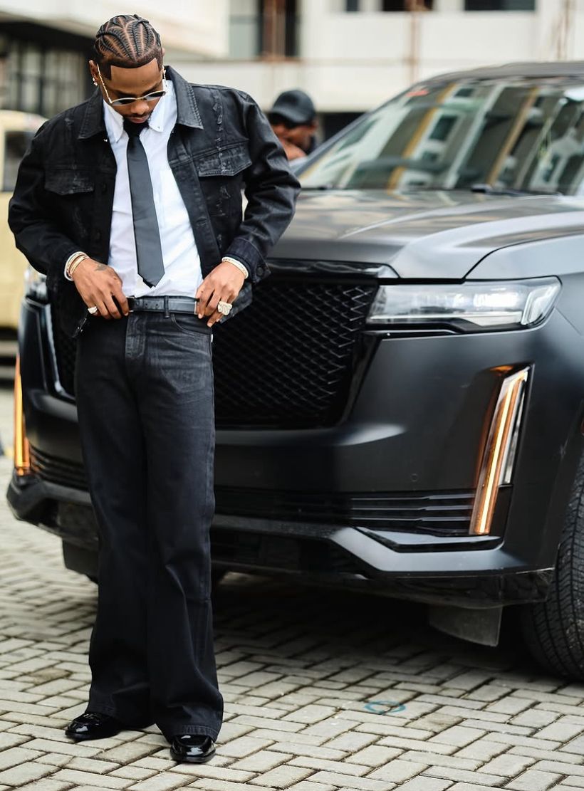 YL in Black Wax Denim Set standing next to a luxury car on a city street.