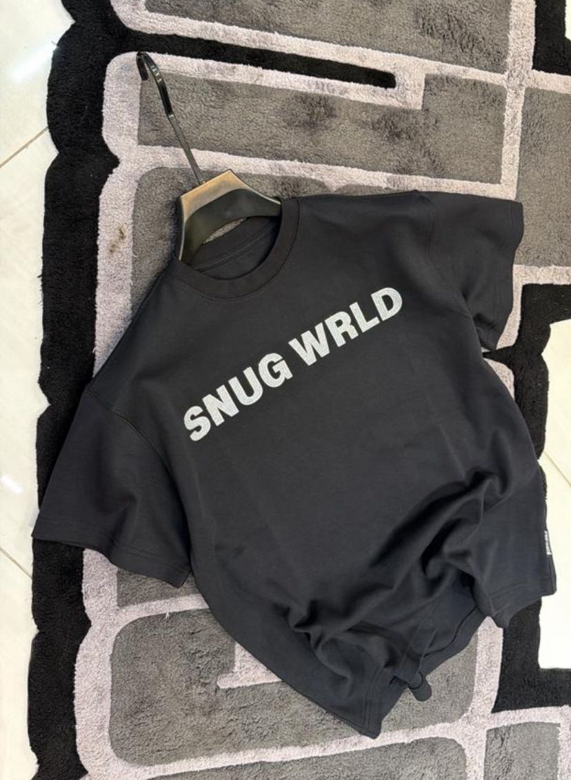 Black sweatshirt with 'SNUG WRLD' text on a textured floor
